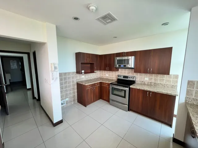 Esquina de cocina con gabinetes de madera oscura, sobres de granito y electrodomésticos de acero inoxidable, además de pisos de baldosas claras.