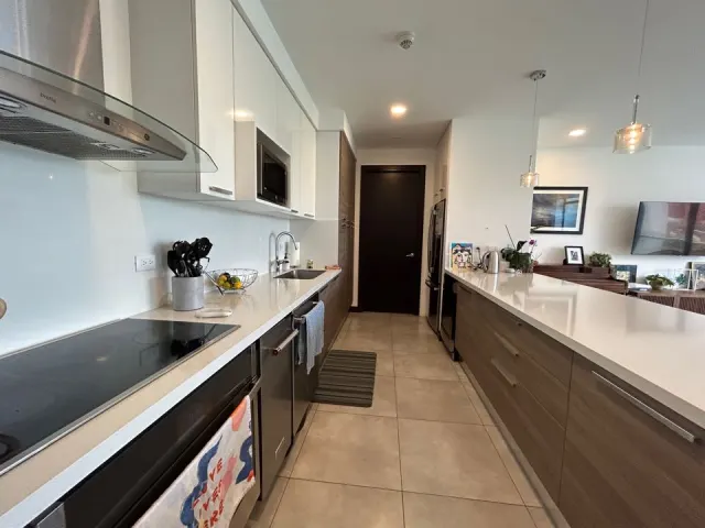 Cocina moderna con encimeras blancas, electrodomésticos de acero inoxidable, gabinetes superiores blancos y gabinetes inferiores de madera.