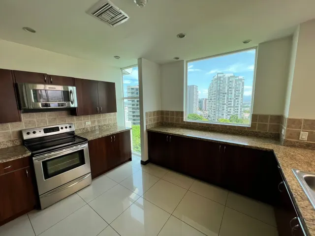 Cocina con gabinetes de madera oscura, sobres de granito, electrodomésticos de acero inoxidable y ventanales con vistas a la ciudad.