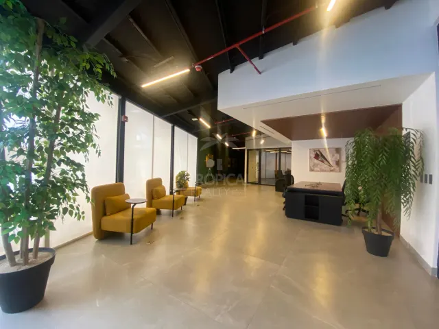 Área de recepción con sillones amarillos y pequeñas mesas auxiliares a lo largo de una pared de vidrio grande, y un escritorio oscuro cerca del fondo.