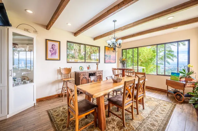 Comedor con mesa de madera y sillas, cielo raso con vigas de madera, vitrina y grandes ventanas con vista al jardín.