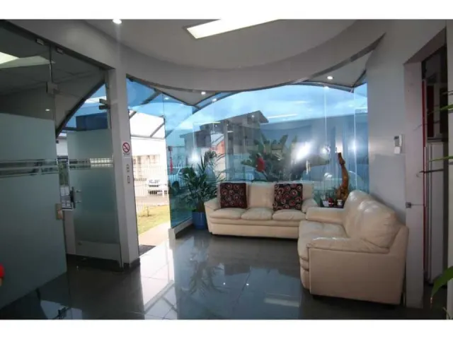 Sala de recepción con pisos de cerámica brillante, una pared de vidrio curva con vista al exterior y dos sofás de cuero blanco.