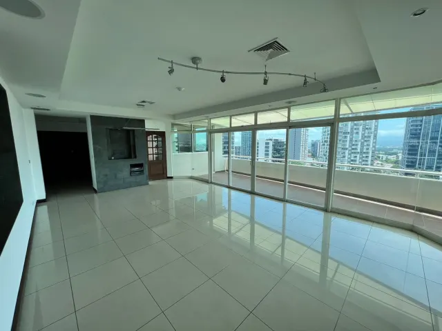 Habitación vacía con pisos de baldosas claras, una pared decorativa de piedra oscura y puertas corredizas de vidrio de piso a techo que abren a un balcón con vistas a la ciudad.