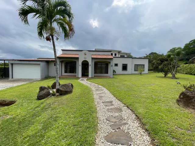 Vista exterior de una casa de una planta que muestra un sendero de piedra y grava hacia la entrada, una palmera en el cesped y un garaje.