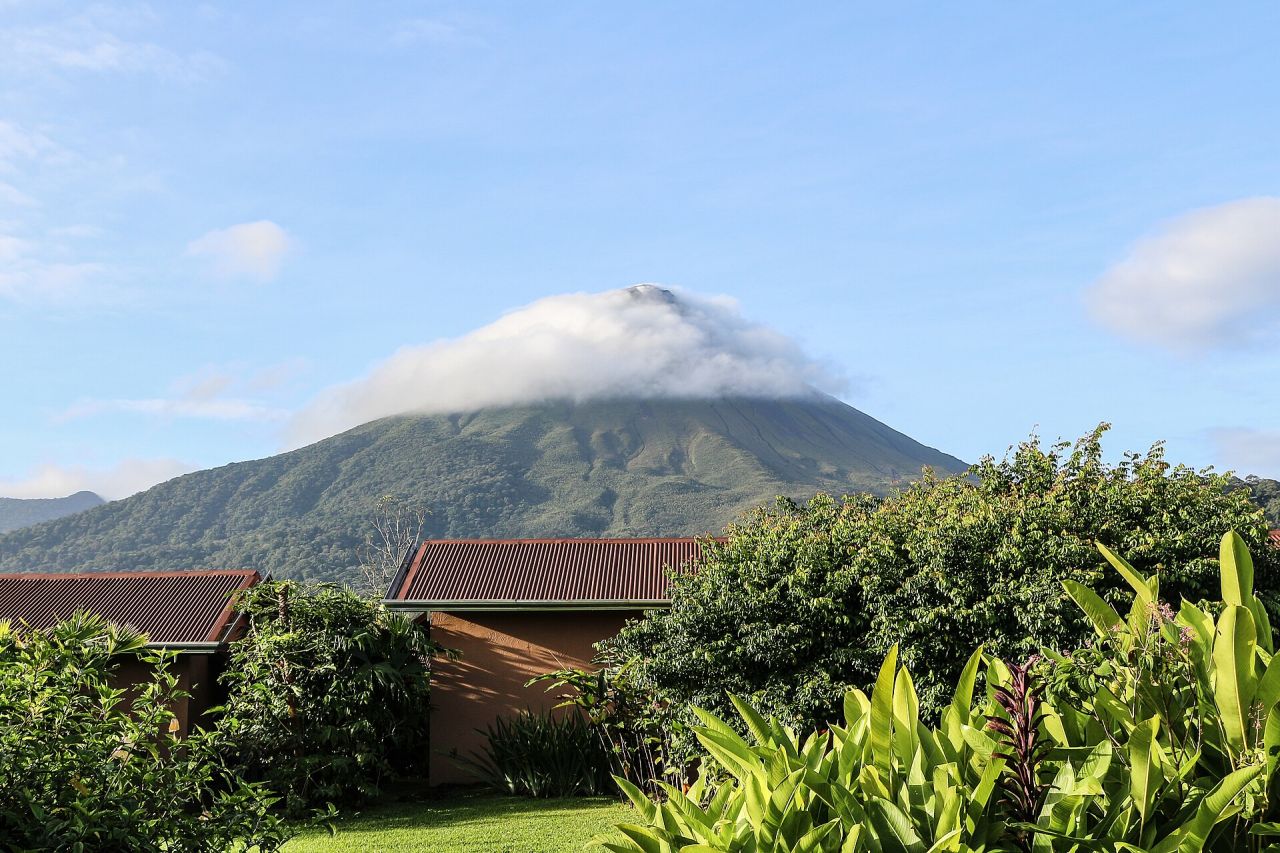 El volcán Arenal con un collar de nubes, visto sobre los techos y jardines de La Fortuna